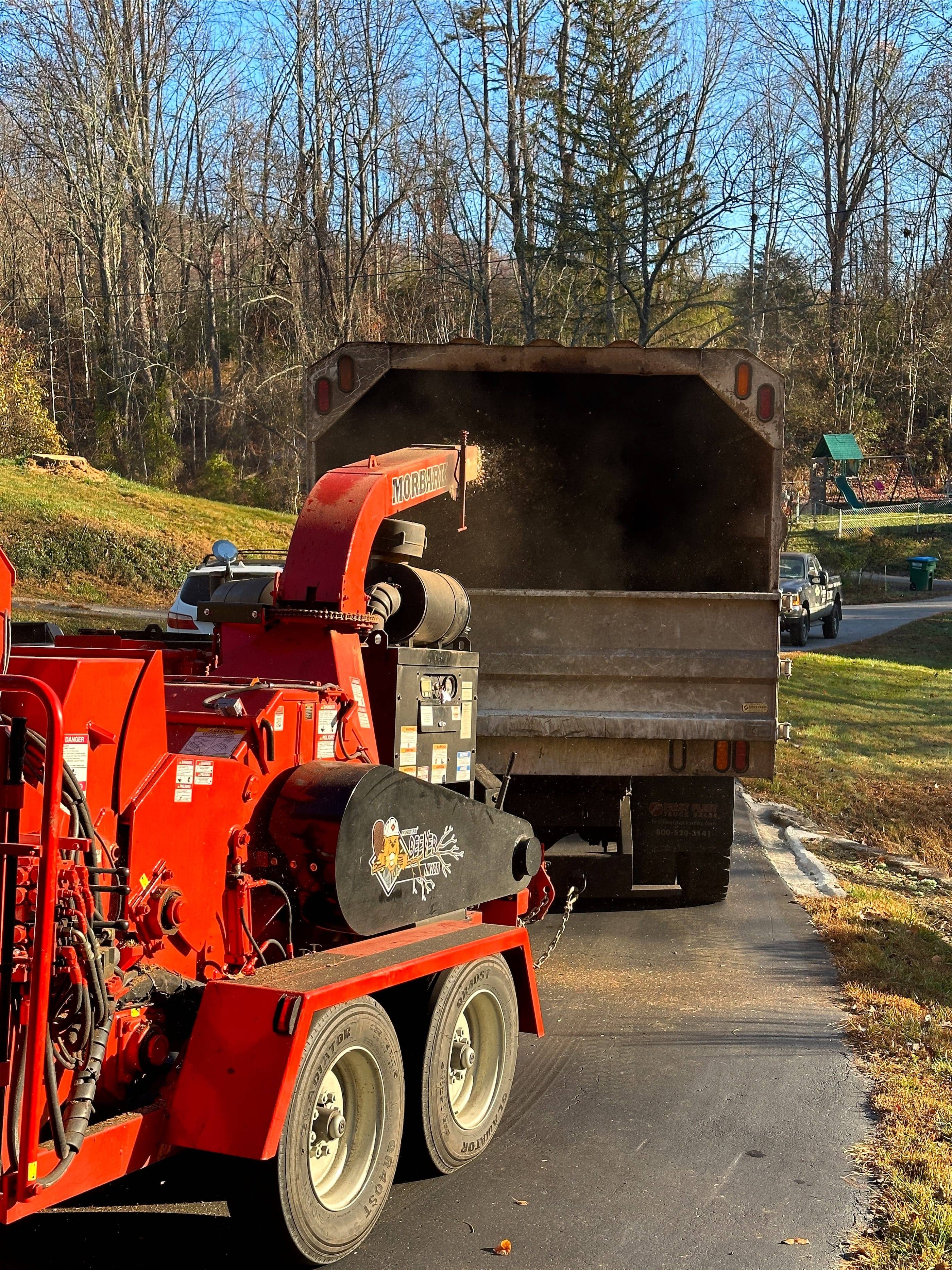 A red tractor pulling a trailer with a chipper attached to it.